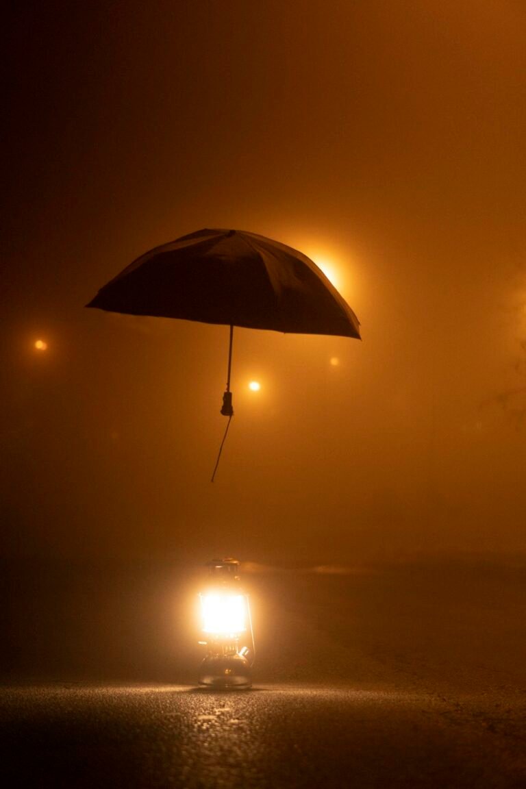 A foggy night scene with a hanging umbrella illuminated by a lantern's glow.